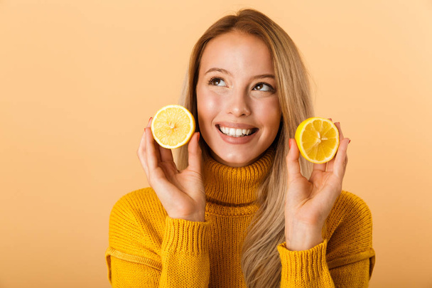 Photo of a beautiful woman holding citrus lemons posing isolated over yellow wall background. - Photo, Image