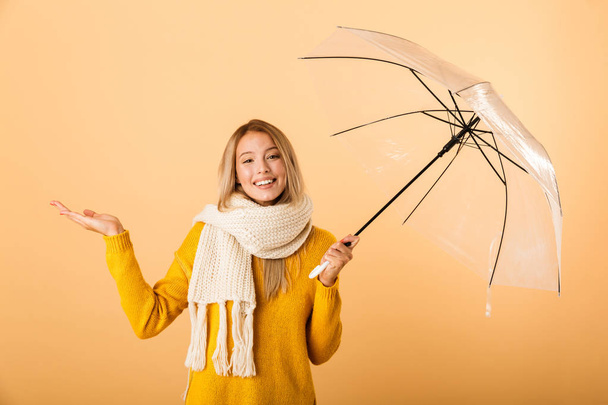 Photo of a cute woman wearing scarf holding umbrella posing isolated over yellow wall background. - Foto, immagini