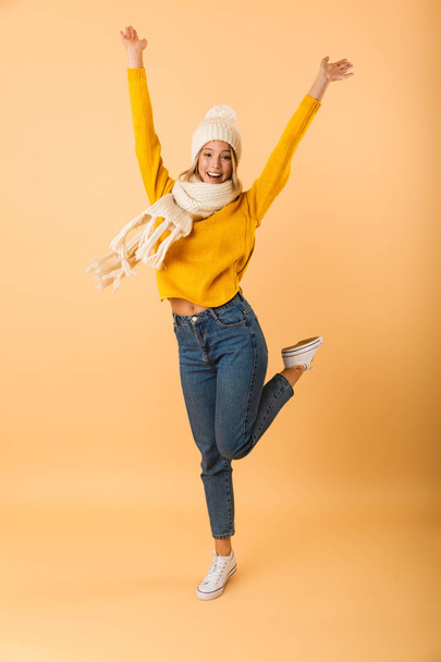 Photo of a cute excited woman wearing scarf and hat posing isolated over yellow wall background. - Foto, Imagen