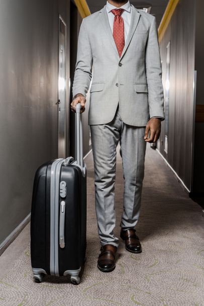 cropped view of businessman with baggage walking in hotel corridor - Foto, imagen
