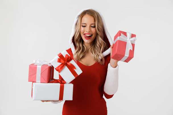 Portrait of a delighted blonde woman dressed in red New Year costume standing isolated over white background, holding stack of present boxes - Foto, immagini