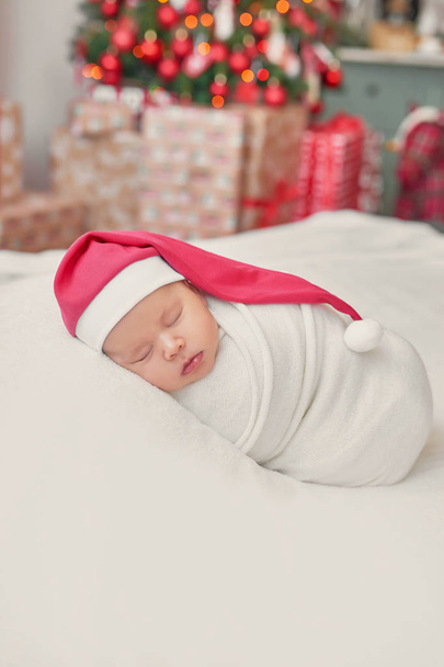 Sleeping, two week old, newborn, baby  wearing  Santa hat. Baby in a Christmas Santa cap.  Cute newborn baby lies swaddled in white blanket. Baby goods packaging template. Healthy and medical concept. - Photo, image