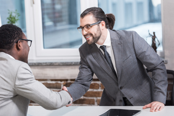 Lächelnde multiethnische Geschäftspartner beim Händeschütteln am Bürotisch - Foto, Bild