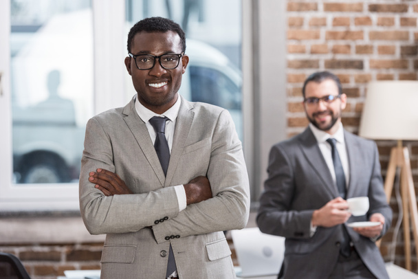 souriant homme d'affaires afro-américain avec les bras croisés regardant caméra et beau partenaire à l'arrière-plan
 - Photo, image