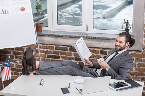 hombre de negocios sonriente sentado en la mesa y poniendo los pies en la oficina
 - Foto, imagen