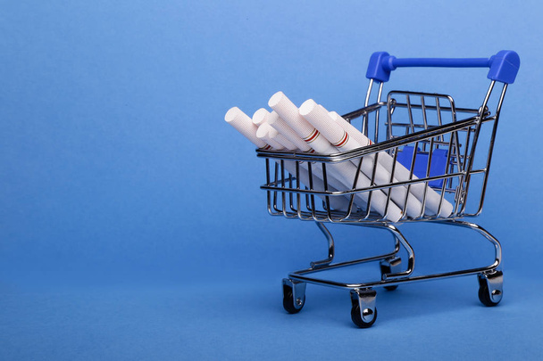 Smoking concept. Cigarettes in shopping cart, shopping trolley on blue background - Fotoğraf, Görsel