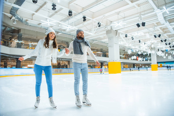 Glückliches Paar hält Händchen beim gemeinsamen Schlittschuhlaufen auf Eisbahn - Foto, Bild