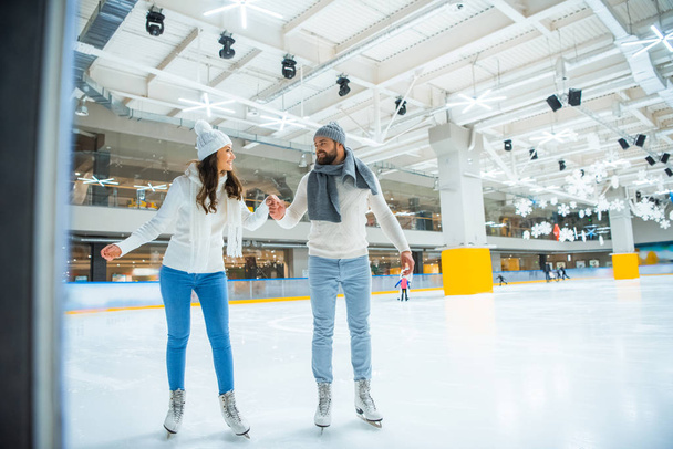 happy couple holding hands while skating on rink together - Фото, зображення