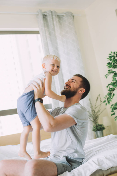 Young father tossing up his little son in the bedroom - Photo, Image