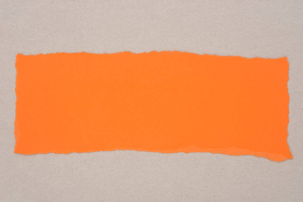 orangefarbenes Stück zerrissenes Papier auf grauem Hintergrund - Foto, Bild