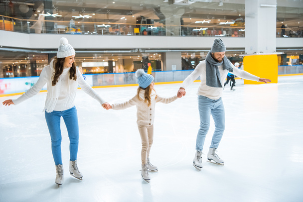 familia en suéteres tomados de la mano mientras patinan juntos en pista de hielo
 - Foto, Imagen