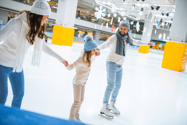 glückliche Familie in Hüten und Pullovern Händchen haltend beim gemeinsamen Schlittschuhlaufen auf der Eisbahn - Foto, Bild