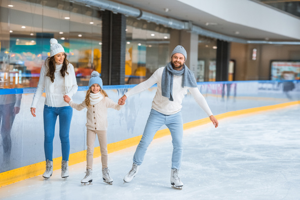happy family holding hands while skating together on ice rink - Foto, imagen