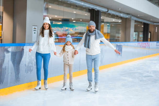 familia feliz tomados de la mano mientras patinan juntos en pista de hielo
 - Foto, Imagen