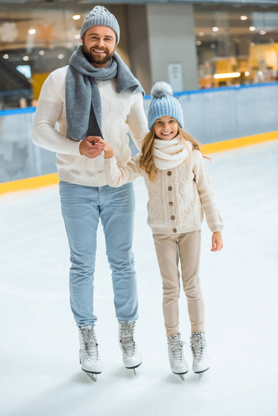 alegre padre e hija tomados de la mano mientras que de pie en pista de patinaje
 - Foto, Imagen