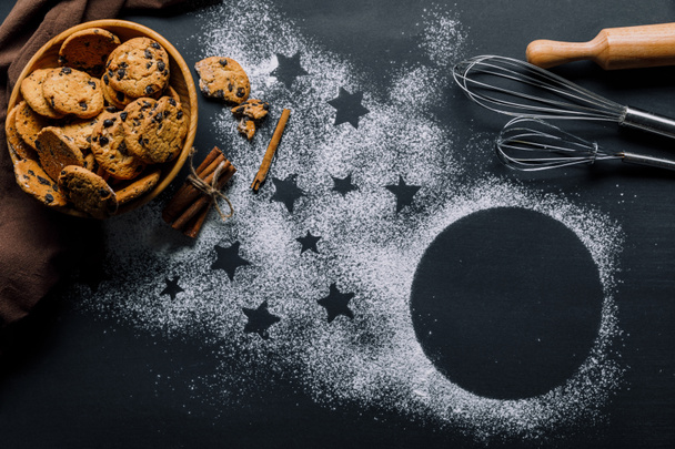 la vista de arriba de las galletas en la escudilla, los batidores y el rodillo sobre la mesa cubierta por la harina con el símbolo de las estrellas
 - Foto, Imagen