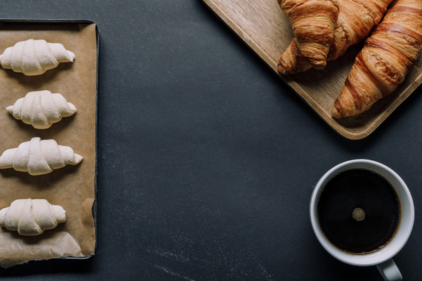 flat lay with coffee cup, dough on tray and croissants on black table - Zdjęcie, obraz