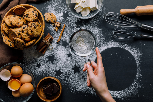 partial view of woman sifting flour through sieve over table covered by flour with symbols of stars and cookies with ingredients - Fotografie, Obrázek