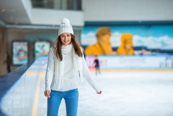 portrait of smiling attractive woman in knitted sweater skating on ice rink alone - Photo, Image
