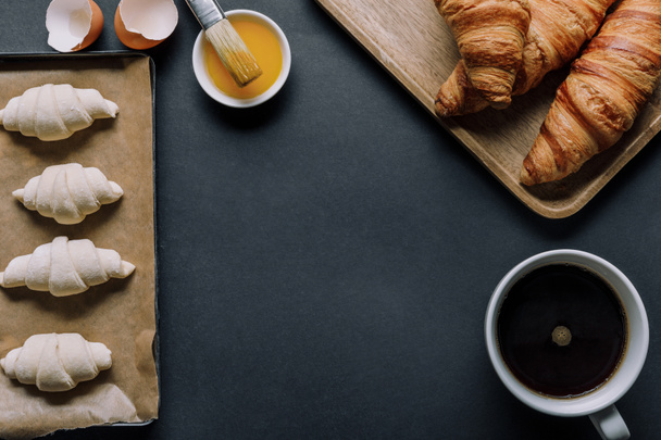 felülnézete a croissant tésztát a tálca, tojássárgája, ecset és a kávé csésze fekete felületen - Fotó, kép