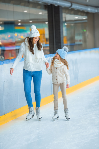 sonrientes madre e hija tomados de la mano y patinando en pista de hielo juntos
 - Foto, Imagen