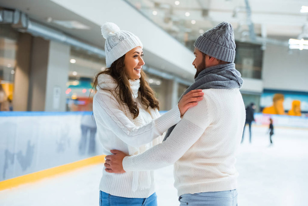 vista lateral de pareja romántica sonriente en pista de patinaje
 - Foto, Imagen
