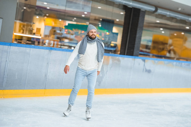 bearded man in knitted hat and sweater skating on ice rink - Photo, image