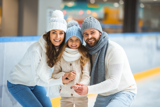 portrait of cheerful parents and daughter in sweaters looking at camera on skating rink - Foto, Imagem
