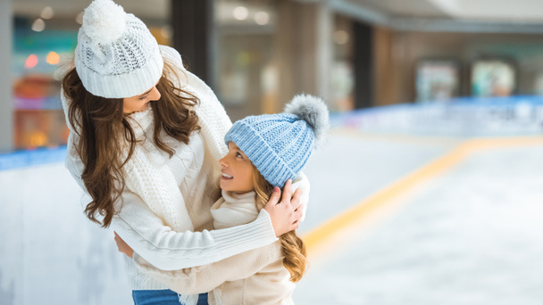 portrait of mother and daughter hugging each other while skating on ice rink together - 写真・画像