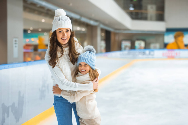 Portret van de moeder en dochter elkaar knuffelen terwijl het schaatsen op de ijsbaan samen - Foto, afbeelding