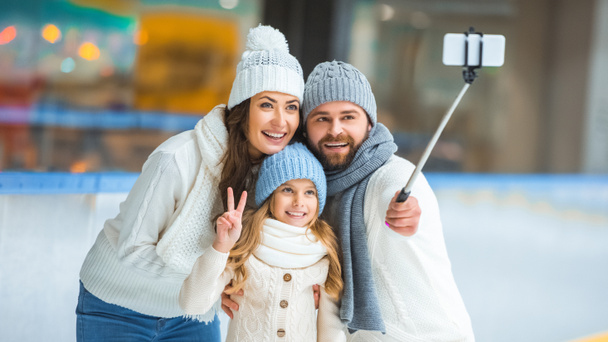 портрет улыбающейся семьи, делающей селфи на смартфоне на катке
 - Фото, изображение