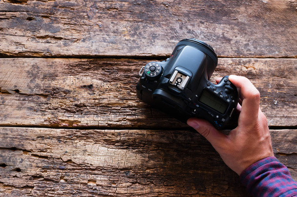 photographer holds a camera on a wooden background with space for text - Foto, Imagen