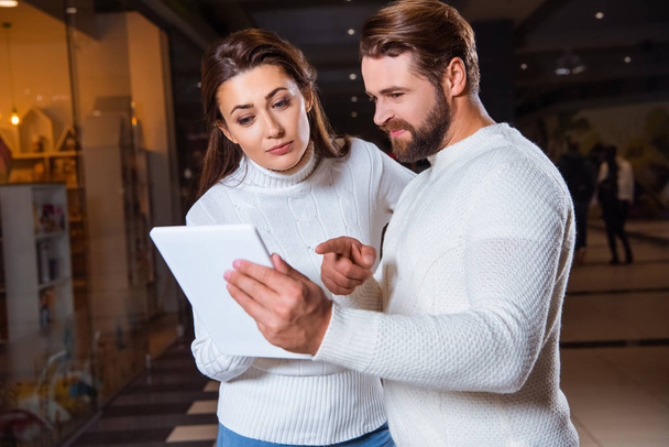 couple in white knitted sweaters using digital tablet together - Foto, Imagen