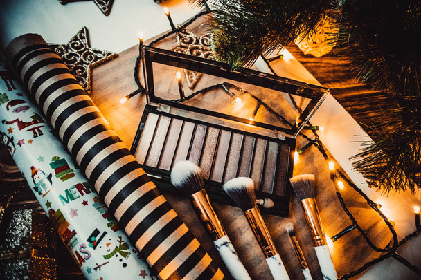 Sombra de ojos con decoraciones navideñas y pinceles de maquillaje sobre fondo marrón madera - Foto, Imagen