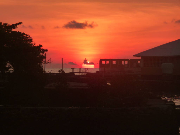 Ρύθμιση του ήλιου στη θάλασσα με κόκκινο ουρανό και σιλουέτα του παράκτιου κτιρίου κατά τη διάρκεια του ηλιοβασιλέματος στην περιοχή Visayas των Φιλιππίνων 2009 - Φωτογραφία, εικόνα