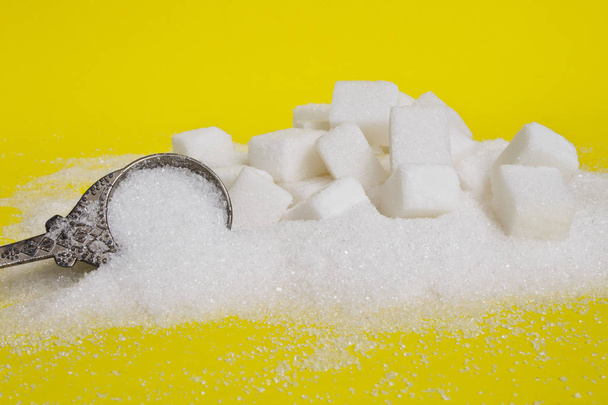 Hintergrund aus Zuckerwürfeln und Zucker in einem Löffel. weißer Zucker auf gelbem Hintergrund. Zucker mit Kopierraum. Seitenansicht oder flache Lage - Foto, Bild