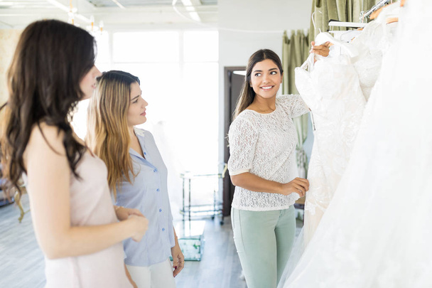 Усміхнена жінка приймає думку про своїх друзів на весільний одяг в магазині
 - Фото, зображення