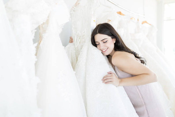 Beautiful bride to be feeling the fabric of her wedding dress in retail store - Foto, imagen