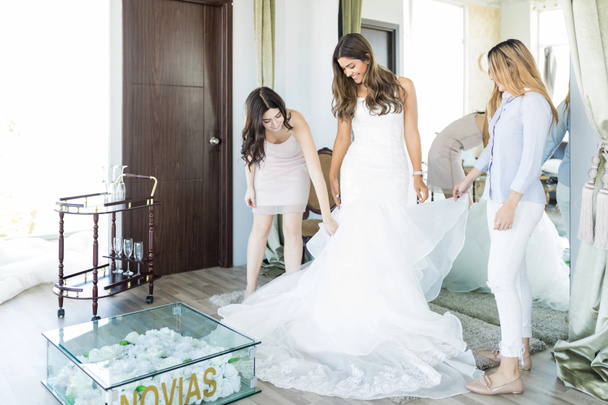Female customers assisting bride with marriage gown while standing in retail shop - Photo, image