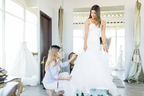 Dressmaker correggere fronzoli di abito da sposa indossato da shopper in studio
 - Foto, immagini