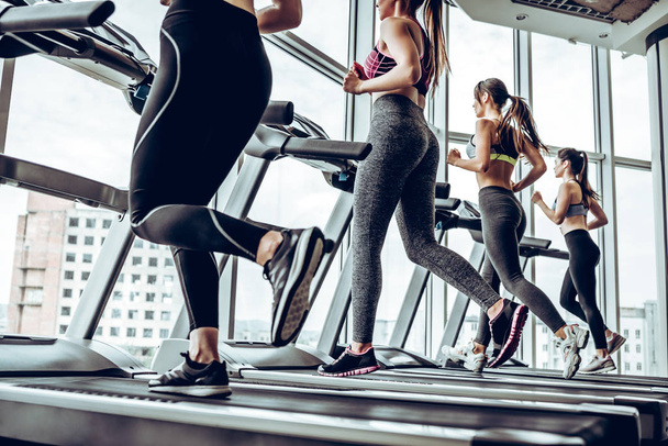 Running together. Side view of young beautiful women looking away while running on treadmill at gym. - Φωτογραφία, εικόνα