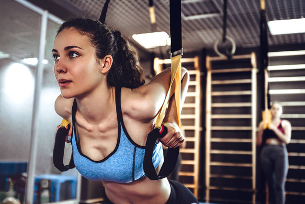 Close up view of young attractive woman does core abs oblique training with fitness straps in the gym. - Fotografie, Obrázek