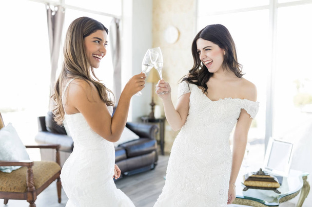 Cheerful and attractive friends in white gowns enjoying party before wedding in boutique - Fotoğraf, Görsel