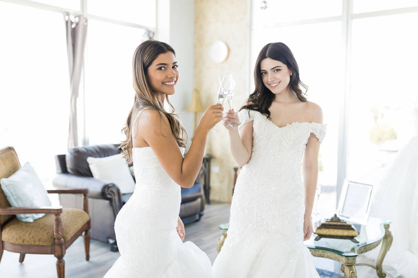 Portrét dvou mnohonárodnostní nevěsty usmívající se přitom šampaňské na přípitek v svatební shop - Fotografie, Obrázek