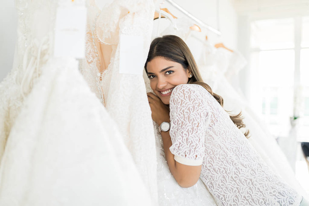 Retrato de sorrir jovem mulher abraçando seu vestido de noiva na loja
 - Foto, Imagem