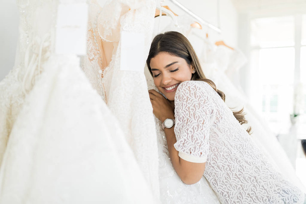 Belle femme hispanique avec les yeux fermés étreignant sa robe de mariée dans le magasin nuptiale
 - Photo, image