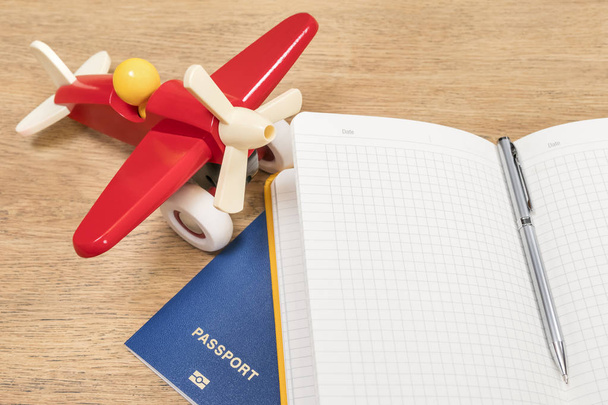 Plane, notebook and passport on wooden table - Φωτογραφία, εικόνα