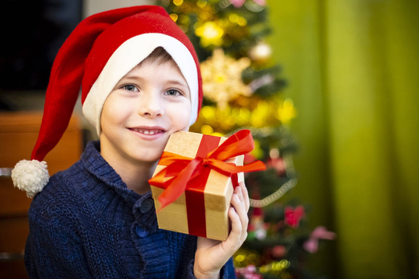 The boy in the hat of Santa Claus to the Christmas tree - Φωτογραφία, εικόνα
