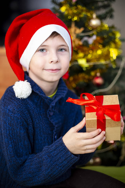 The boy in the hat of Santa Claus to the Christmas tree - Φωτογραφία, εικόνα