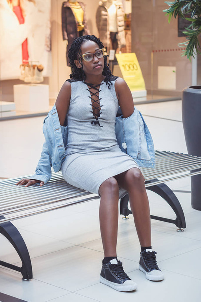 Young dark-skinned woman dressed in casual clothes on the bench in the mall, blurred background - Foto, immagini